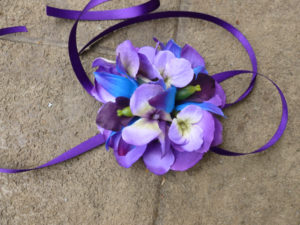 Purple and blue wrist corsage made with purple hydrangeas, galaxy orchids, purple ribbon ties, royal blue, royal purple
